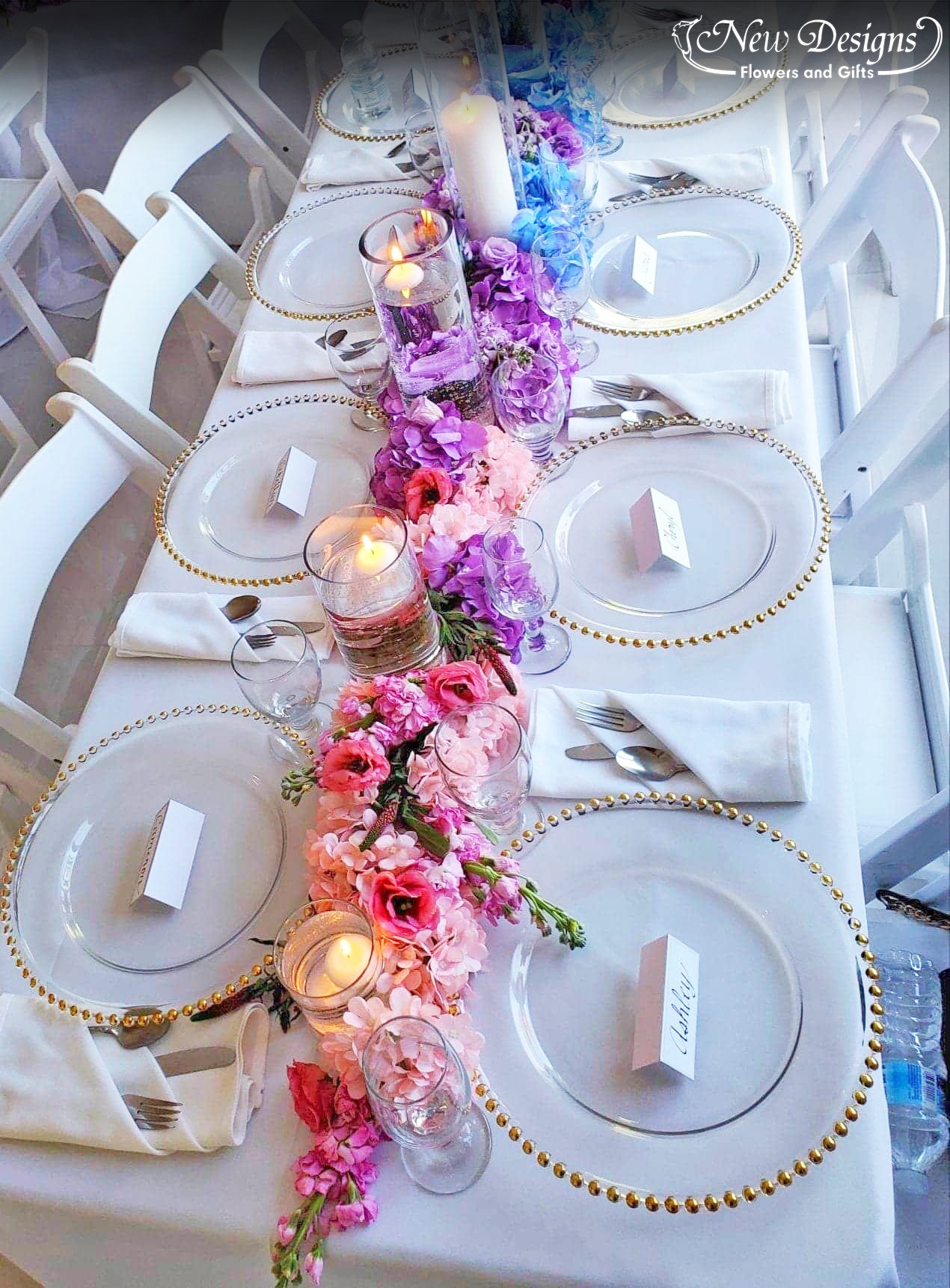 A Garland runs down the center of a crisp home table setting, of full lush hydrangeas in an ombre orientation, flowing seamlessly from Pink to Purple to Blue